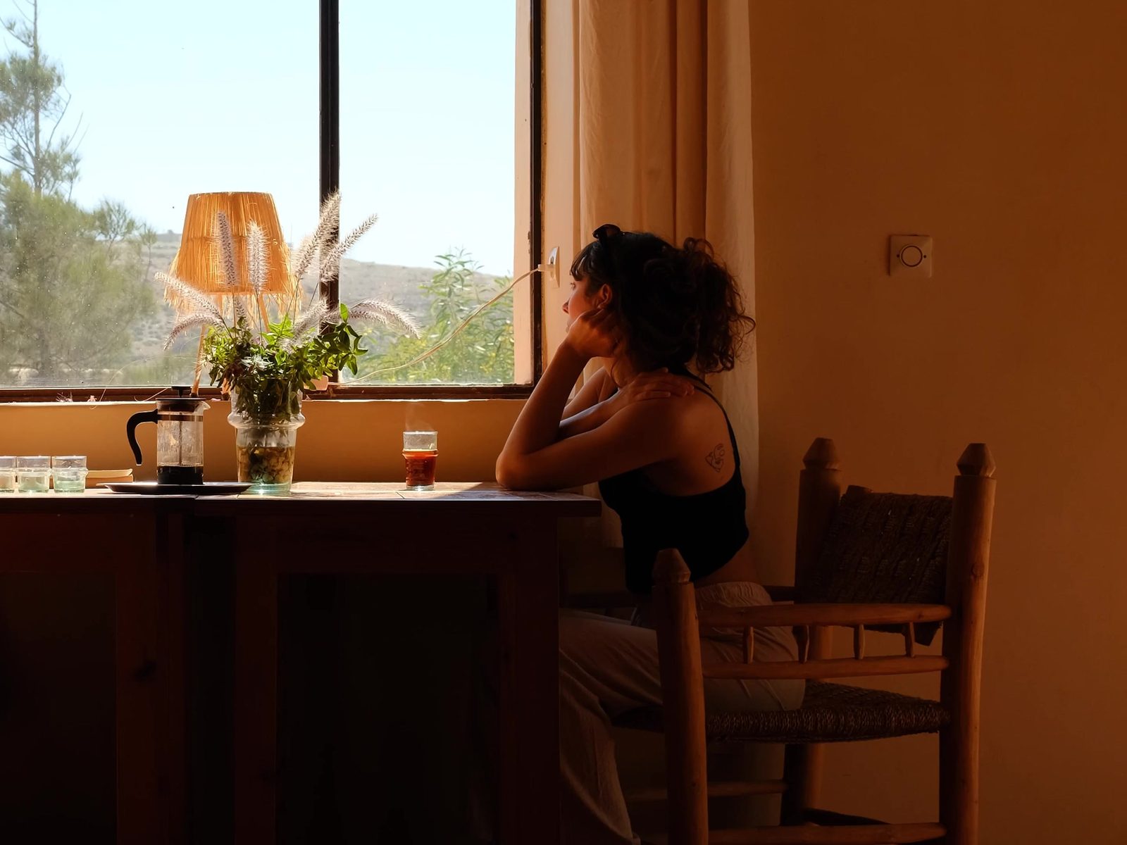 A woman at her breakfast table resting her head on her hand, looking out at the early morning light